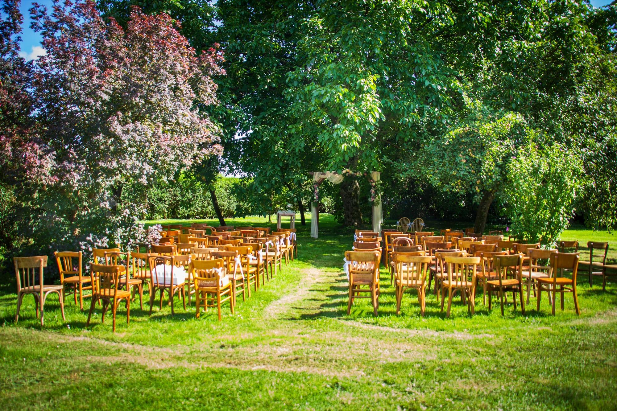 Chaises en bois disposées en arc de cercle sous les grands arbres