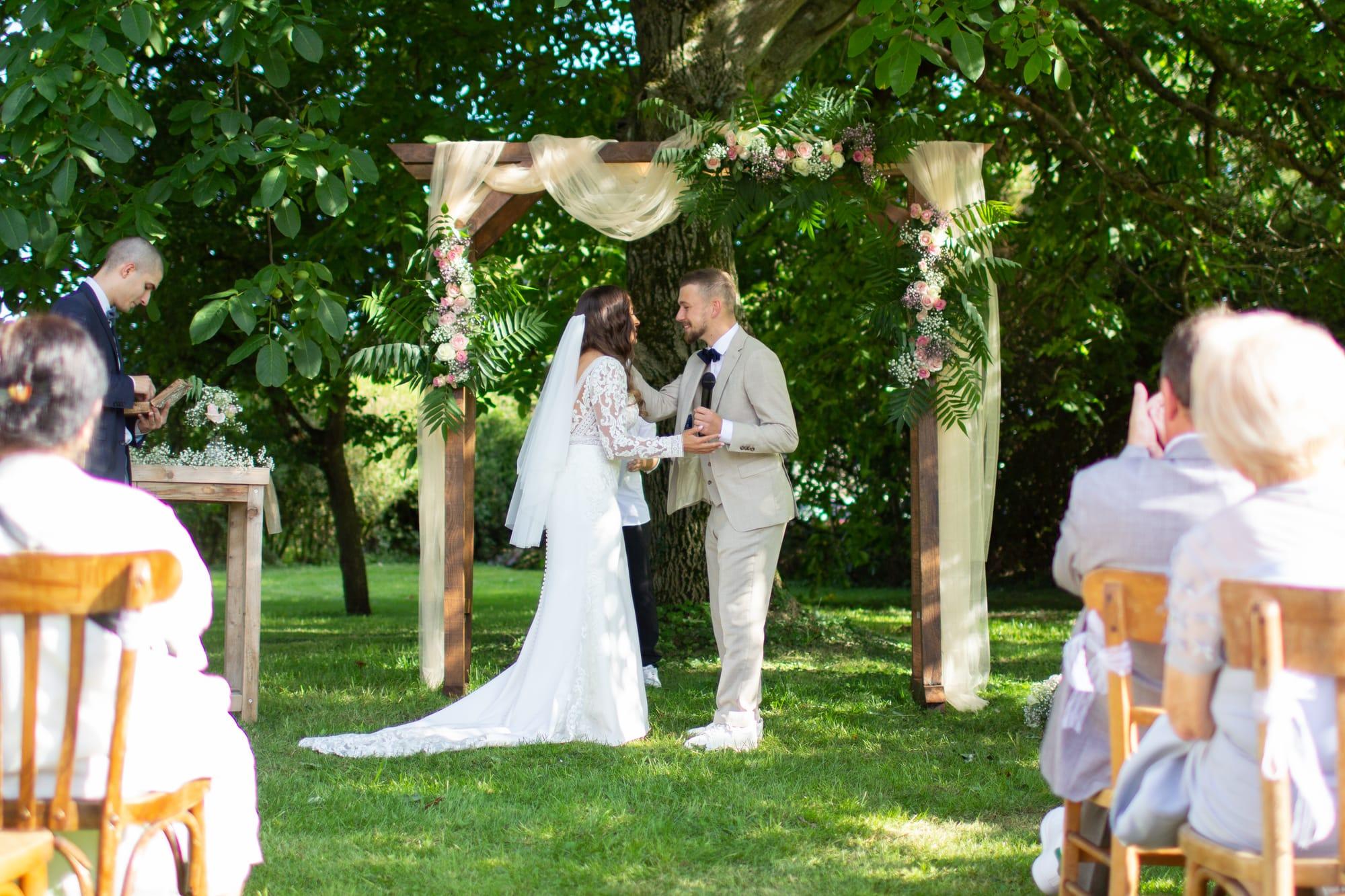 Les mariés sous l’arche fleurie devant leurs invités